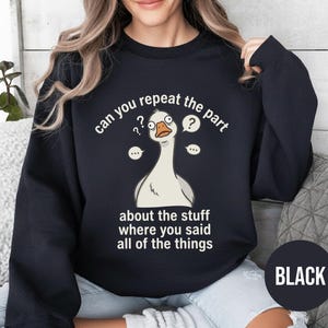 Puede incluir: Sudadera negra con una ilustraci&oacute;n de un ganso de dibujos animados y bocadillos. El texto de la sudadera dice "can you repeat the part about the stuff where you said all of the things". La palabra "BLACK" est&aacute; en un c&iacute;rculo en la parte inferior.
