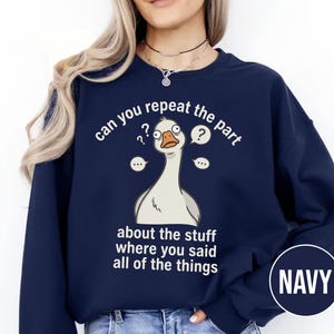 Puede incluir: Sudadera azul marino con una ilustraci&oacute;n de un ganso de dibujos animados y el texto "can you repeat the part about the stuff where you said all of the things." La palabra "NAVY" est&aacute; en un c&iacute;rculo en la parte inferior derecha.