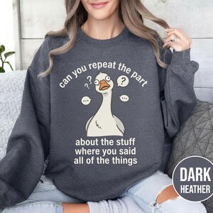 Puede incluir: Sudadera gris oscuro con una ilustraci&oacute;n de un ganso de dibujos animados y el texto "can you repeat the part about the stuff where you said all of the things." La sudadera tambi&eacute;n tiene el texto "DARK HEATHER".