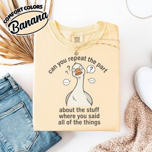 Puede incluir: Camiseta amarillo claro con un dibujo de un ganso y el texto "can you repeat the part about the stuff where you said all of the things". La camiseta tambi&eacute;n tiene las palabras "COMFORT COLORS" y "Banana".