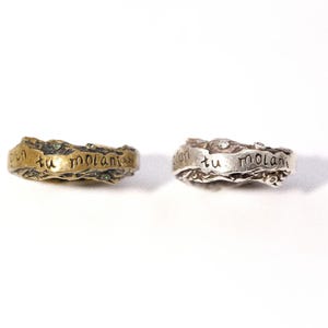 May include: Two textured rings, one gold-toned and one silver-toned, are displayed on a white background. Each ring has the phrase "con tu molani" engraved on its surface. The rings have a unique, organic design.