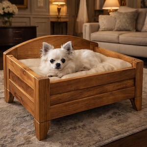 Puede incluir: Un perro pequeño y blanco descansa cómodamente en una cama para perros de madera. La cama es de madera marrón claro con un cabecero curvado y un cojín beige suave. El perro es de raza de pelo largo, probablemente un chihuahua, con ojos oscuros.