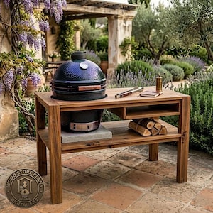 Op de afbeelding: Een donkergroene keramische kamado-grill met een houten handvat en een temperatuurmeter staat op een rechthoekige houten tafel. De tafel heeft een onderste plank met gestapeld brandhout, een zijvak en een metalen kruidenmolen bovenop.