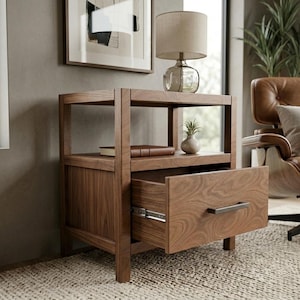 Puede incluir: Una mesita de noche de madera con un cajón abierto. La mesa tiene un estante con un libro y un pequeño jarrón. Una lámpara está encima. La mesa es de madera con un acabado natural. El cajón tiene un tirador metálico.