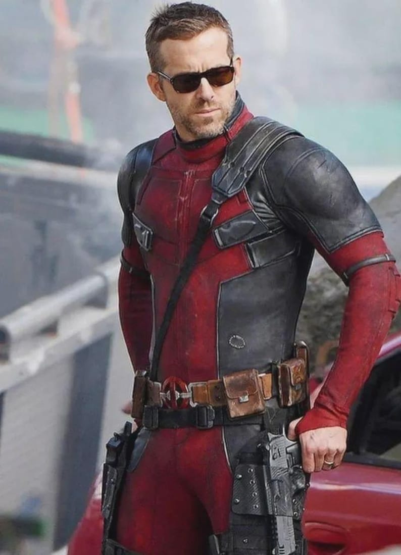 Puede incluir: Una persona con un traje t&aacute;ctico rojo y negro de acabado texturizado, un cintur&oacute;n utilitario de cuero marr&oacute;n con hebilla circular y fundas negras con pistolas. El conjunto incluye gafas de sol oscuras y una correa al hombro.