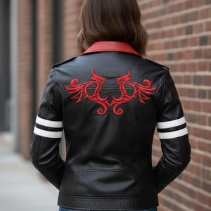 May include: A black leather jacket featuring a red collar, red embroidered dragon-like motifs on the upper back, and two horizontal white stripes on each sleeve. The jacket is worn over blue denim jeans, showcasing a structured fit and design.