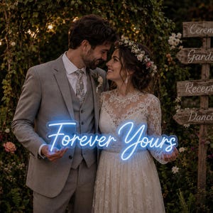 May include: A bright blue neon sign featuring the cursive text Forever Yours. The sign is held by two individuals, one wearing a grey suit with a vest and tie, and the other wearing a white lace long-sleeve dress with a floral headpiece.