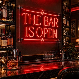 May include: A rectangular neon sign mounted on a dark wall with the glowing red text THE BAR IS OPEN, featuring decorative flourishes above and below the lettering. The sign is secured with four silver hardware mounts on a clear acrylic backing.