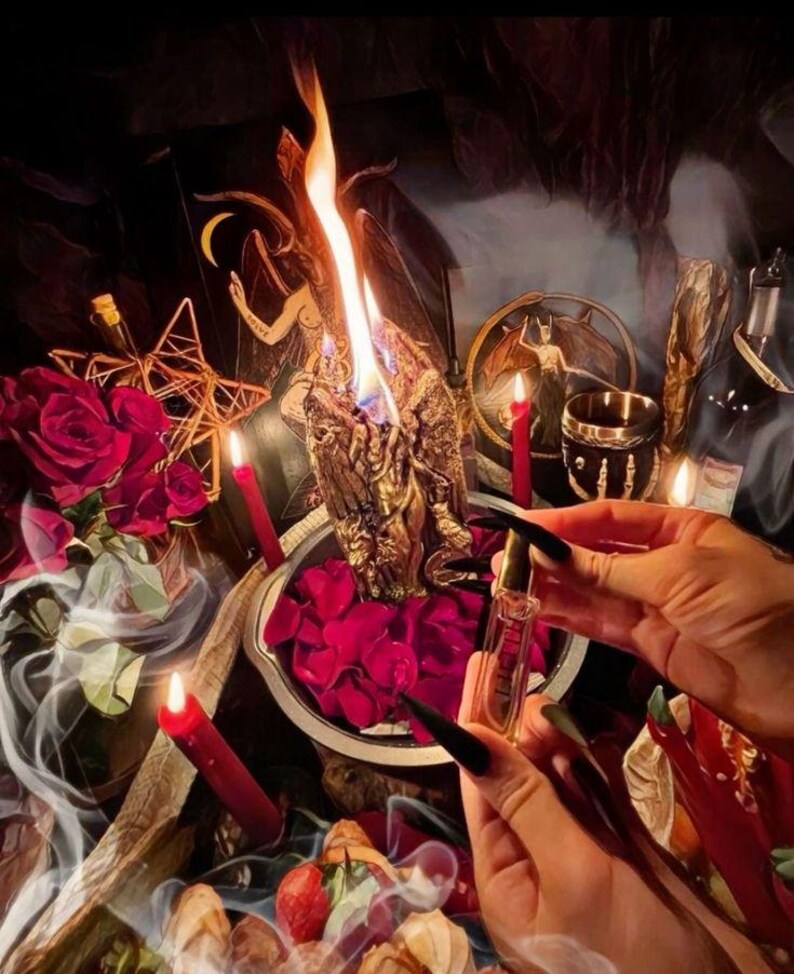 May include: A mystical scene featuring a lit gold candle with a detailed figure, surrounded by red roses, candles, and a small vial held by a person. The image has a dark, atmospheric aesthetic with a focus on ritualistic elements.