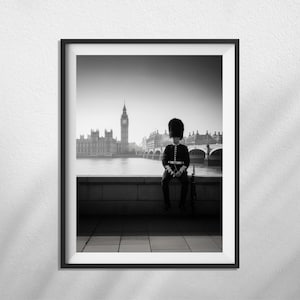 May include: Black and white framed print of a British Royal Guard sitting on a wall with the Houses of Parliament and Big Ben in the background. The guard is wearing a traditional uniform and bearskin hat.