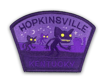 Può includere: Toppa ricamata viola con il testo "Hopkinsville, Kentucky" e un'illustrazione di tre creature nere con occhi gialli luminosi su uno sfondo di cielo notturno viola con stelle e una luna crescente.