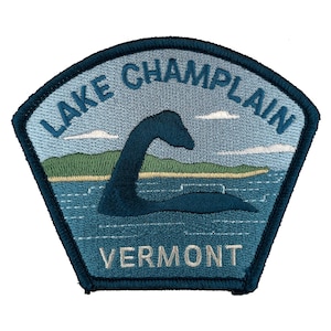 May include: A blue and green embroidered patch with the text "Lake Champlain Vermont" and a silhouette of the lake monster Champy.
