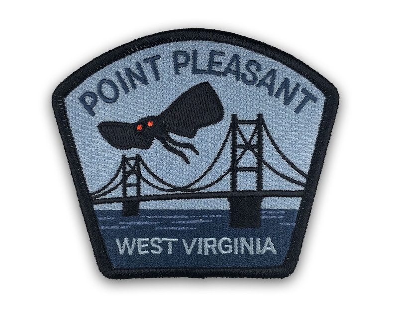 May include: A blue and black embroidered patch with the text "Point Pleasant, West Virginia". The patch features a silhouette of a bridge and a flying creature with red eyes.