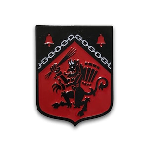 May include: A black and red enamel pin featuring a black devil-like creature holding a pitchfork and a shield with a chain border. The creature is standing on a red background with two bells at the top.