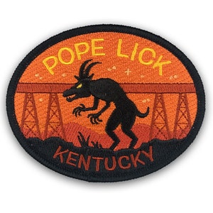 May include: An embroidered patch with an orange background and black outline. The patch features a black silhouette of a creature with horns and a bridge in the background. The text "Pope Lick Kentucky" is embroidered in yellow on the patch.