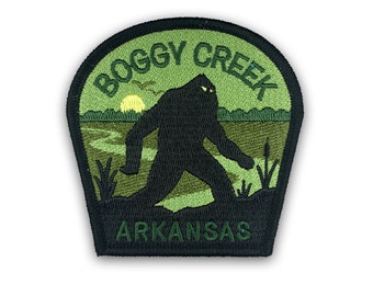 May include: Green and black embroidered patch with a silhouette of Bigfoot walking through a swamp. The text "BOGGY CREEK ARKANSAS" is embroidered around the image.