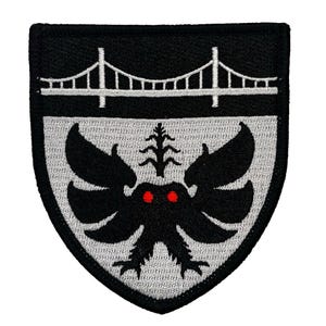 May include: Black and white embroidered patch with a gray shield shape. The shield features a black creature with red eyes and a white bridge at the top.