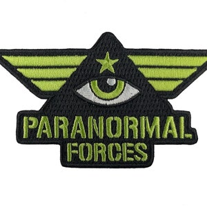 Może przedstawiać: Czarna i zielona naszywka haftowana ze stylizowanym okiem, skrzydłami i tekstem "PARANORMAL FORCES".
