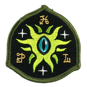 May include: Embroidered patch with a black background and a green border. The patch features a central design of a green eye with blue iris, surrounded by green rays. Gold symbols and white crosses are also present.