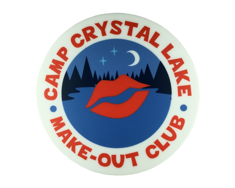 以下が含まれることがあります： 「Camp Crystal Lake Make-Out Club」と赤い文字で書かれた白い丸いボタン。ボタンは青い背景に赤い唇のグラフィック、三日月、星が描かれている。