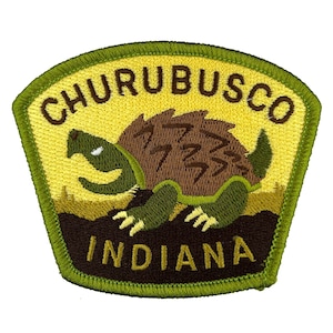 May include: A yellow and green embroidered patch with a cartoon snapping turtle and the text "Churubusco Indiana".