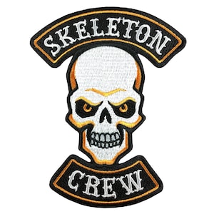 May include: Black and white embroidered patch with a white skull and crossbones design. The skull has yellow eyes and a black mouth. The text "SKELETON CREW" is embroidered in white on a black background with a yellow outline.