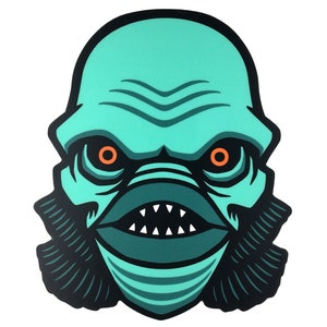 May include: A teal green monster face with orange eyes and sharp teeth. The monster has gills and a textured skin.