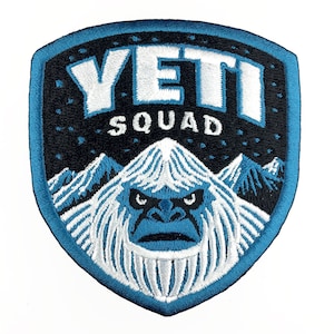 May include: A blue and white embroidered patch with the text "YETI SQUAD" and a Yeti monster with a blue face in the centre.