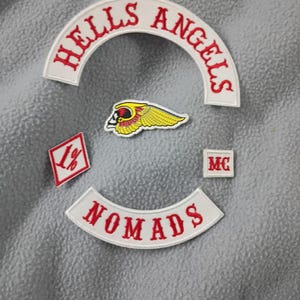 May include: A collection of embroidered patches featuring the words "HELLS ANGELS" in red on a white arched background. Other patches include a winged skull, the word "NOMADS", "1%", and "MC".