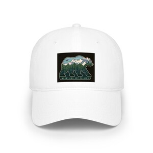 May include: White baseball cap with a black square patch featuring a bear silhouette filled with a mountain and forest scene. The text "MOUNTAINS ARE CALLING" is printed below the bear.