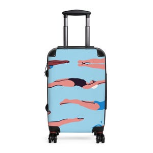 Könnte beinhalten: Ein hellblauer Rollkoffer mit einem Muster von Schwimmern in verschiedenen Badeanzügen. Die Schwimmer sind in einem minimalistischen Stil mit rosa Gliedmaßen und schwarzen oder blauen Badeanzügen dargestellt. Der Koffer hat einen schwarzen Griff und Räder.