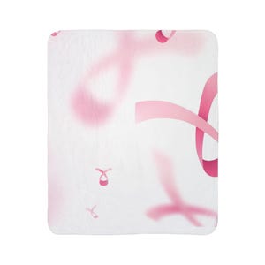 Puede incluir: Una manta blanca con un patrón de lazos rosas, algunos enfocados y otros borrosos, creando un diseño suave y reconfortante. Los lazos son un símbolo de la concienciación sobre el cáncer de mama.