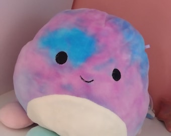 Könnte beinhalten: Ein rundes Plüschtier mit einem Batikmuster in Blau, Lila und Pink. Das Spielzeug hat einen cremefarbenen Bauch, zwei kleine schwarze runde Augen und ein einfaches, aufgesticktes schwarzes Lächeln. Es hat mehrere weiche, abgerundete Gliedmaßen.