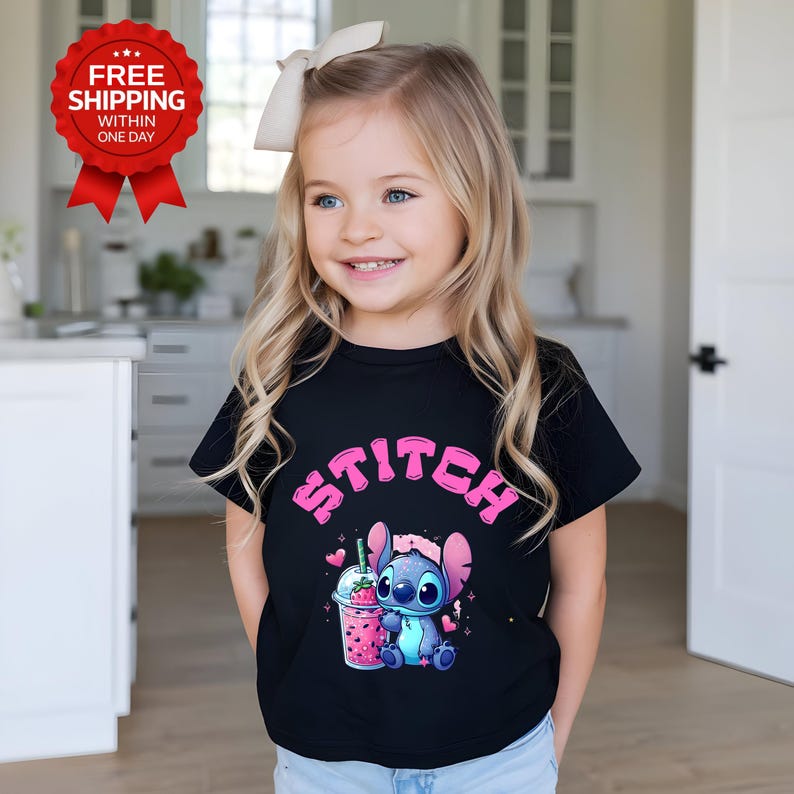 K&ouml;nnte beinhalten: Ein schwarzes T-Shirt mit dem Wort "STITCH" in rosa Buchstaben. Das T-Shirt zeigt eine Zeichentrickfigur, die ein Getr&auml;nk mit Erdbeermuster h&auml;lt. Das Bild zeigt ein junges M&auml;dchen, das das T-Shirt tr&auml;gt.
