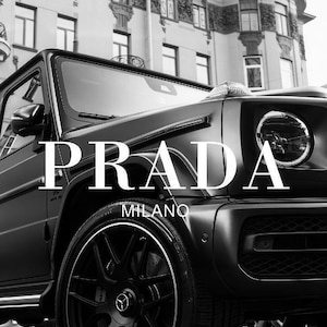 Peut inclure: Image en noir et blanc d'un SUV de luxe avec le logo Prada et le texte "Milano". Le véhicule a des jantes et des pneus noirs et est garé devant un bâtiment.