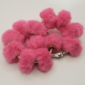 May include: A set of pink fluffy accessories, possibly for a costume or novelty item. The items are connected by silver-colored metal rings and clasps. The fluffy material is a vibrant, saturated pink.
