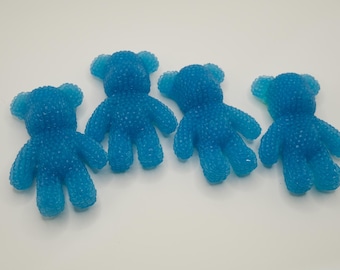 May include: Four small, translucent blue bear-shaped figures with a textured, bumpy surface. Each bear features rounded ears, short arms, and legs, arranged in a horizontal row. The material appears semi-transparent with a consistent bright blue color throughout the entire set of four identical bear-shaped objects.