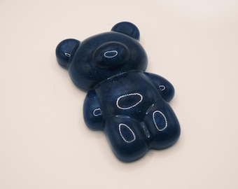 May include: A dark blue, glossy, bear-shaped object with a smooth, rounded surface. The bear features a distinct head with two small ears, a rounded snout, and a body with defined limbs. The finish has a subtle, shimmering, glitter-like texture.