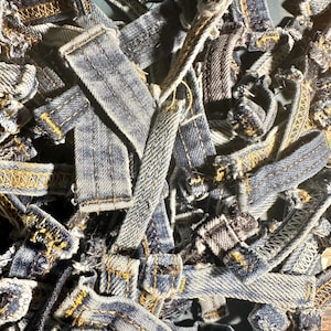 Może przedstawiać: Zbliżenie na stos skrawków materiału dżinsowego. Skrawki mają różne kształty i rozmiary, z postrzępionymi krawędziami i widocznymi żółtymi szwami. Dżins jest w kolorze wyblakłego niebieskiego, z widocznymi śladami zużycia.