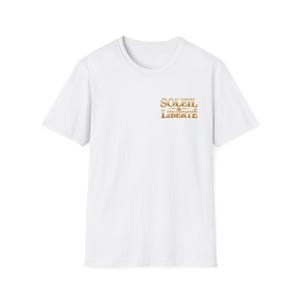 Peut inclure: T-shirt blanc à manches courtes. Le t-shirt présente les mots "SOLEIL & LIBERTÉ" en lettres dorées sur le haut de la poitrine gauche. Le t-shirt est fait d'une matière douce et confortable.