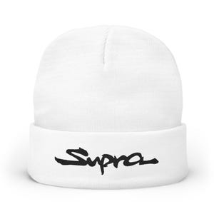 May include: A white beanie hat with a folded brim. The word "Supra" is printed in black, stylized script across the brim. The hat is made of a knitted material.
