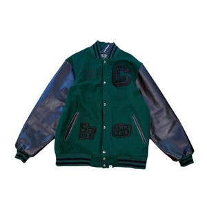 May include: A green varsity jacket with black leather sleeves and black ribbed cuffs. The front features a large black letter C patch, a patch with the number 57, and a patch with the text CWB 2018. It has a snap button closure and a stand-up collar.
