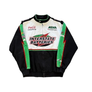 May include: A black, white, and green racing jacket with the "Interstate Batteries" logo on the front. The jacket features sponsor logos like "Coca-Cola" and "MBNA Pontiac". The jacket has a zip-up front and a stand-up collar.
