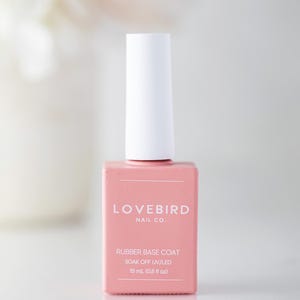 May include: A pink Lovebird Nail Co. rubber base coat nail polish bottle with a white cap. The bottle has the text "RUBBER BASE COAT" and "SOAK OFF UV/LED". The bottle contains 15 ml (0.5 fl oz) of product.