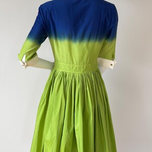 Puede incluir: Vestido vibrante con bloques de color. El corpi&ntilde;o presenta un degradado de azul y verde, y la falda es verde. Tiene cuello y pu&ntilde;os blancos, y una cintura entallada. Las mangas son de tres cuartos.