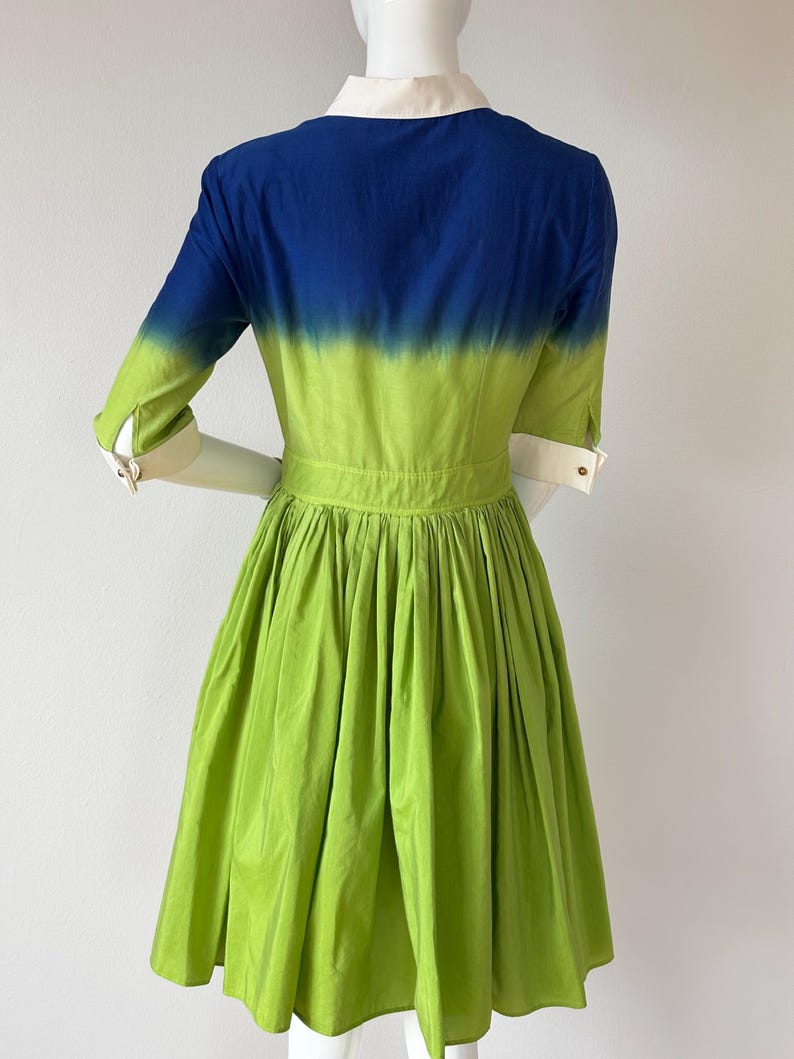 Puede incluir: Vestido vibrante con bloques de color. El corpi&ntilde;o presenta un degradado de azul y verde, y la falda es verde. Tiene cuello y pu&ntilde;os blancos, y una cintura entallada. Las mangas son de tres cuartos.
