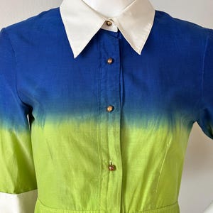 Puede incluir: Vestido degradado azul y verde con cuello blanco y botones. El vestido presenta mangas cortas con pu&ntilde;os blancos y una falda plisada. El degradado de color pasa del azul al verde, creando un dise&ntilde;o vibrante y llamativo. El vestido mide unos 100 cm de largo.