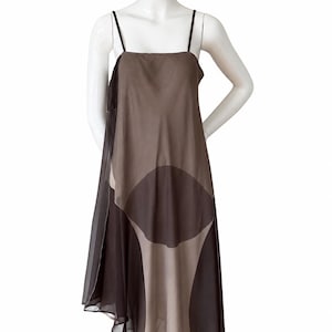 Puede incluir: Un vestido midi sin mangas con escote cuadrado y tirantes finos. La prenda está confeccionada en un tejido transparente superpuesto en tonos topo y marrón oscuro, mostrando un gran patrón geométrico circular en la parte delantera.