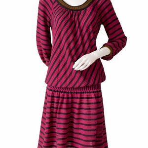 May include: A two-piece outfit on a mannequin. The top and skirt are a vibrant pink with black diagonal stripes. The neckline and sleeve cuffs have a brown trim. The skirt has an elastic waistband. The outfit is made of a soft, flowing fabric.