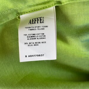 Puede incluir: Primer plano de una etiqueta blanca con el nombre de la marca "AEFFE" impreso, adherida a una tela verde brillante. La etiqueta proporciona detalles de la composici&oacute;n de la tela en varios idiomas.